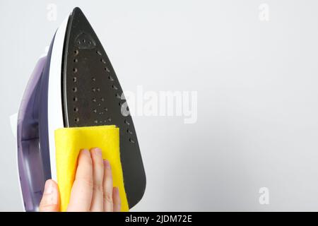 La femme au foyer essuie la surface sale du fer à repasser avec un chiffon jaune. Nettoyage du fer des dépôts de carbone. Banque D'Images
