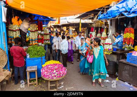 Mysore, Karnataka, Inde : les femmes marchent devant les étals de fleurs au marché de Devaraja. Banque D'Images