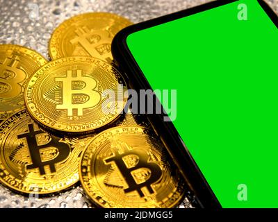 Pièces de monnaie Bitcoin en métal doré avec un téléphone intelligent à côté de lui, espace de copie de zone d'écran vert Banque D'Images