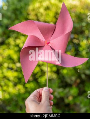 Une main mâle tient une pinwheel rouge maison contre un fond vert flou avec des lumières de bokeh Banque D'Images