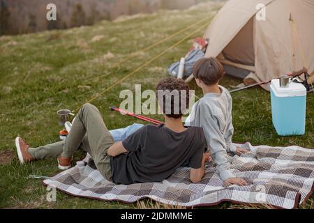 Arrière sur l'homme et la femme allongé sur l'herbe à la tente dans les montagnes et profitant de la vue depuis le sommet. Banque D'Images