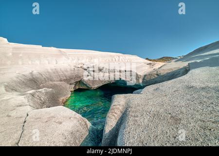 Rochers blancs uniques et eau verte émeraude dans la grotte de mer, plage de Sarakiniko, île de Milos, Grèce. Falaises vides, soleil d'été, ciel bleu clair Banque D'Images