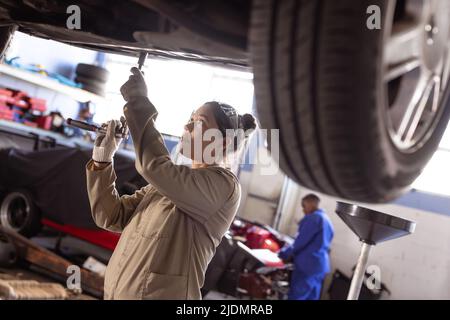 Femme asiatique moyenne à l'aide d'une clé lors de la réparation de la voiture en atelier Banque D'Images