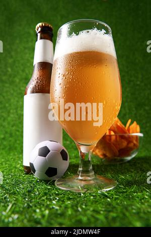 Bouteille et verre de bière sur fond d'herbe verte. Concept de fan de football Banque D'Images