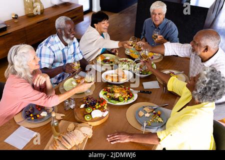 Vue en grand angle des amis séniors multiraciaux qui toaster les lunettes de vin à la table de la maison de soins infirmiers Banque D'Images