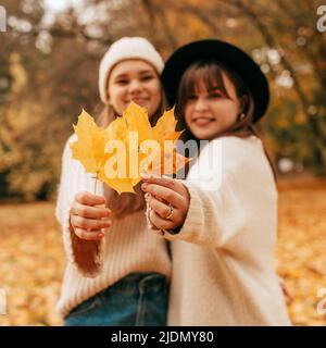 Deux jeunes femmes, non focalisées en arrière-plan, tiennent les feuilles d'érable jaune dans leurs mains et les tiennent à l'appareil photo. Automne doré. Vacances Banque D'Images