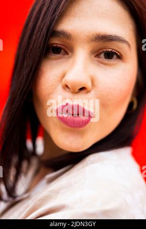 Portrait d'une jeune femme brune envoyant un baiser à l'appareil photo, sur fond rouge Banque D'Images