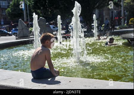 ZAPORIZHHIA, UKRAINE - 20 JUIN 2022 - Un garçon est assis sur le rebord d'une fontaine en été, Zaporizhzhia, dans le sud-est de l'Ukraine. Cette photo ne peut pas être dist Banque D'Images