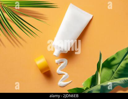 Tube cosmétique blanc avec crème solaire et texture crème pressée sur fond orange. Banque D'Images