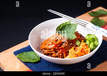 Food concept korean Spice Cold sarrasin Noodle Kimchi Bibim Guksu sur bois et fond noir avec espace de copie Banque D'Images