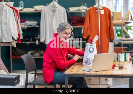 Femme à la machine à coudre parlant à l'écran d'ordinateur portable Banque D'Images