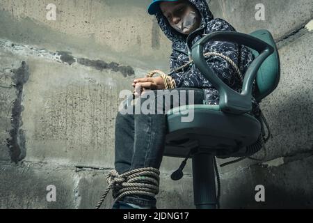 un enfant au sous-sol est assis sur une chaise attachée avec une corde Banque D'Images