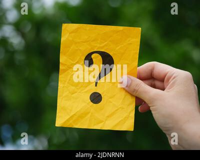 Une femme portant un papier note jaune avec un point d'interrogation dans sa main sur un fond de feuillage. Gros plan. Banque D'Images