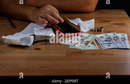 Argent dans une main, chèques sur la table avec de l'argent, un homme compte ses dépenses sur une calculatrice Banque D'Images