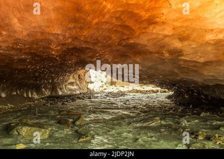 Grotte de glace orange sculptée dans le glacier de Vallelunga traversé par un ruisseau Banque D'Images