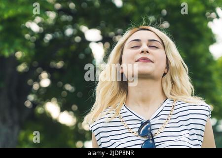 Gros plan moyen d'une jeune fille blonde de race blanche qui profite de l'air frais en été. Fond vert à l'extérieur. Photo de haute qualité Banque D'Images