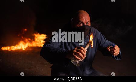 Un homme masqué tient une bouteille brûlante. Cocktail Molotov. Banque D'Images