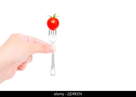 Main tenant une fourchette miniature avec un petit cocktail de tomate sur le dessus isolé sur fond blanc. Concept lié au régime et aux troubles de l'alimentation. Banque D'Images