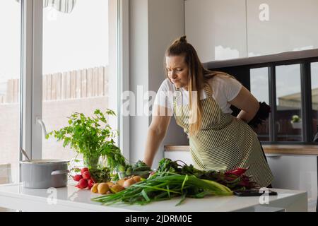 Une femme blonde de grande taille cuisant des aliments sains dans la cuisine, en choisissant une salade de légumes, de la verdure. Vie végétarienne Banque D'Images