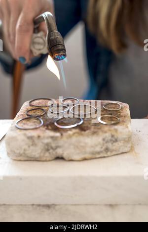 gros plan des mains de bijoutier travaillant avec un chalumeau sur des bijoux en argent dans son atelier. Banque D'Images