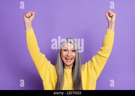 Photo de gaie riant mature femelle élever des poings dans la victoire gagner le prix de loterie isolé sur fond violet couleur Banque D'Images