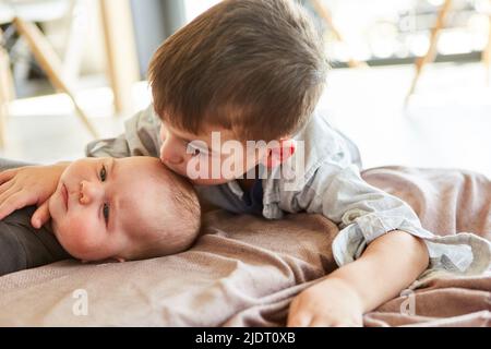 Petit garçon comme grand frère donne à bébé un baiser sur le front pour l'amour et l'affection Banque D'Images