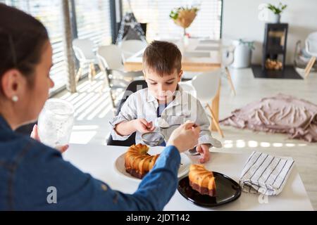 Enfant aidant la mère à cuire le gâteau dans la cuisine avec le sucre en poudre dans la passoire sur le gâteau de marbre Banque D'Images
