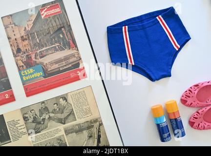 23 juin 2022, Brandebourg, Eisenhüttenstadt: Une paire de troncs de natation de VEB Strickwaren Oberlungwitz à partir de 1970s, des chaussures de bain 'Carola' et un spray solaire 'Violetta' sont exposés dans l'exposition 'frontières de l'amitié. Tourisme entre le GDR, le CSSR et la Pologne' au Centre de documentation pour la culture quotidienne du GDR. Le « Rideau de fer » a traversé l'Europe pendant la Guerre froide, mais les frontières entre les « pays amis » socialistes étaient aussi une question politique et ne pouvaient être passables que dans une certaine mesure. En 1960s, ils sont devenus un peu plus perméables, mais l'année 1972 a marqué un réel Banque D'Images