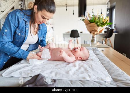 La mère change la couche de bébé sur la table à langer à la maison dans le salon Banque D'Images