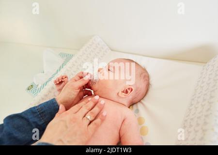 La mère soignante donne à son bébé une sucette pour plus de confort sur la table à langer Banque D'Images