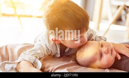 Fier grand frère donnant le baiser de frère de bébé sur le front à la maison Banque D'Images