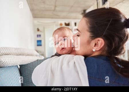 Mère donne à son bébé un baiser tendre sur la joue à la maison dans le salon Banque D'Images