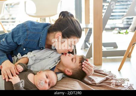 Une mère heureuse se câliner avec deux enfants et donner un baiser affectueux à son grand frère Banque D'Images