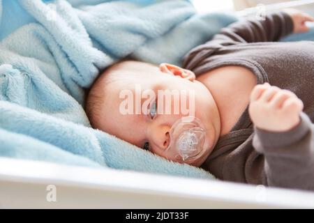 Bébé mignon avec sucette repose paisiblement dans le lit et regarde attentivement Banque D'Images