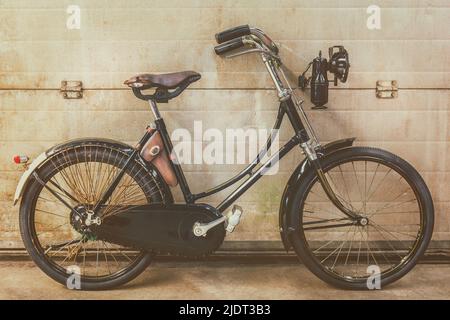 Vélo noir vintage pour femmes garées dans une ancienne usine avec des portes en acier Banque D'Images