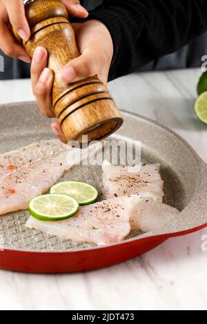 Femme moulin à la main poivre sur filet poisson sur une poêle à l'aide de moulin à poivre en bois, gros plan sur Dori filet Banque D'Images