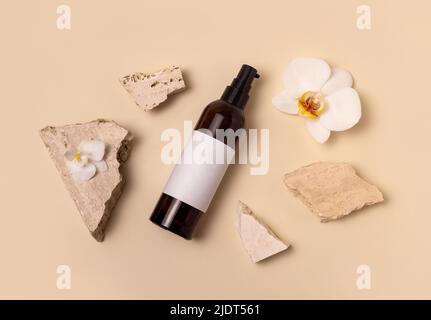 Bouteille de maquillage en verre foncé près des fleurs d'orchidées blanches et des pierres sur le jaune clair, vue de dessus, maquette. Produit de beauté, tonique ou lotion fait main pour le soin de la peau. Banque D'Images