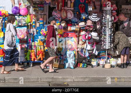Les vacanciers qui marchent devant un étalage coloré de jouets et de nouveautés de plage devant une boutique de Newquay, en Cornouailles, au Royaume-Uni. Banque D'Images