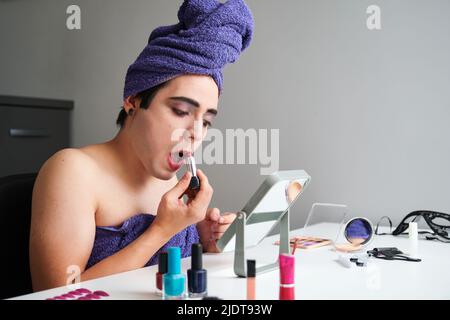 Jeune homme transgenre appliquant le rouge à lèvres. Banque D'Images