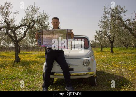 Homme consultant un plan de route penché contre une voiture d'époque après avoir été perdu pendant des vacances en Italie Banque D'Images