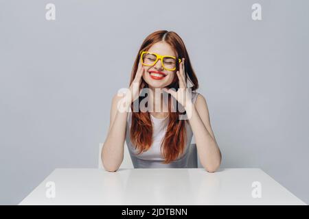 Laughing Caucasian woman sitting at table portant des lunettes jaunes Banque D'Images