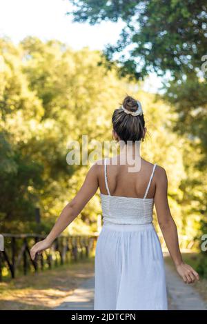 Vue verticale de la jeune femme brune portant une coiffure de pain sur une tenue de boho lors d'une chaude journée d'été dans les bois Banque D'Images