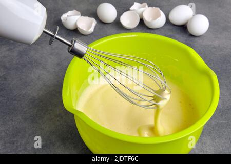 Battez les œufs avec du sucre et de la farine dans un bol vert et un fouet pour fouetter sur une table en béton foncé le fond d'une coquille d'œuf. Maison bi Banque D'Images