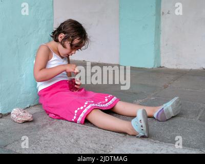 Une jolie fille est assise sur le sol en pierre et mange des framboises mûres d'une tasse. Copier l'espace. Banque D'Images