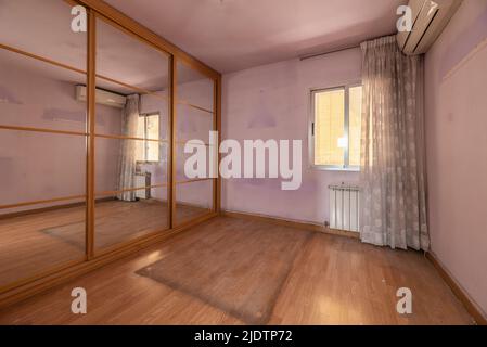 Chambre vide avec armoire avec portes coulissantes à miroirs, fenêtre avec rideaux de fleurs, climatisation et parquet en chêne clair Banque D'Images