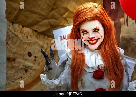 Pattensen, Allemagne, 4 juin 2022 : une jeune jolie femme habillée de clown maléfique avec un visage peint en blanc étire sa main avec de longs ongles de fantaisie Banque D'Images