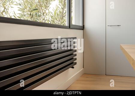 Détail d'un radiateur noir moderne sous la fenêtre d'une cuisine Banque D'Images