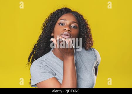 Belle fille afro-américaine avec la coiffure afro sourit joyeusement et envoie un baiser d'air sur un fond jaune Banque D'Images