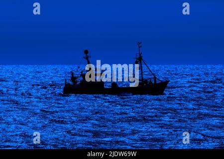 Chalutier de fond, bateau de pêche naviguant le long de la côte de la mer du Nord silhoueté contre le ciel bleu de nuit en face de Nieuwpoort / Nieuport, Flandre, Belgique Banque D'Images