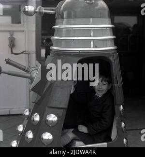 1967, historique, un jeune garçon assis dans un Dalek, Angleterre, Royaume-Uni. Une race extraterrestre fictive de mutants ou de robots, les Daleks sont apparus pour la première fois dans le programme de télévision de science-fiction Briitsh Doctor Who en 1963. Créé par Terry Nation, les Daleks sont rapidement devenus le personnage le plus populaire du BBC. Les extraterrestres ont été conçus par Raymond Cusick, qui, en tant qu'employé salarié de la BBC à l'époque, n'a reçu aucun des revenus générés par les marchandises Daleks, contrairement à Nation qui l'a fait, tout comme un auteur de script indépendant. Banque D'Images